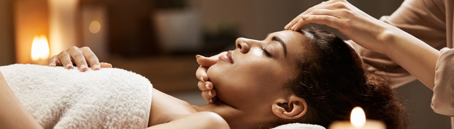 Femme recevant un massage du visage et du crâne dans un spa à la lueur des bougies